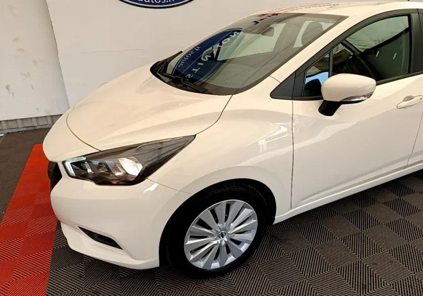 Vue 3/4 avant droit d'une Nissan Micra blanche 2022 avec phares allumés et jantes alliage visibles.