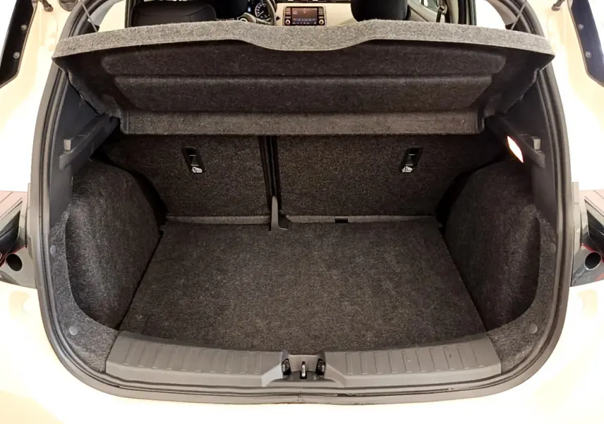 Coffre ouvert d'une Nissan Micra blanche, vue arrière montrant l'espace de chargement et la tablette de protection relevée.