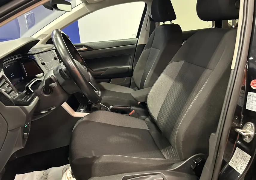 Vue intérieure côté conducteur de la Volkswagen Polo noire 2022, montrant sièges tissu et tableau de bord avec écran digital.