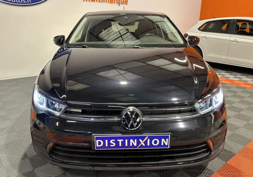 Vue avant d'une Volkswagen Polo noire 2022 avec phares allumés et calandre chromée dans un showroom.
