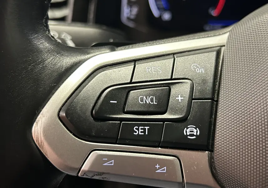 Gros plan sur les commandes au volant côté gauche d’une Volkswagen Polo noire, avec boutons de régulateur de vitesse.