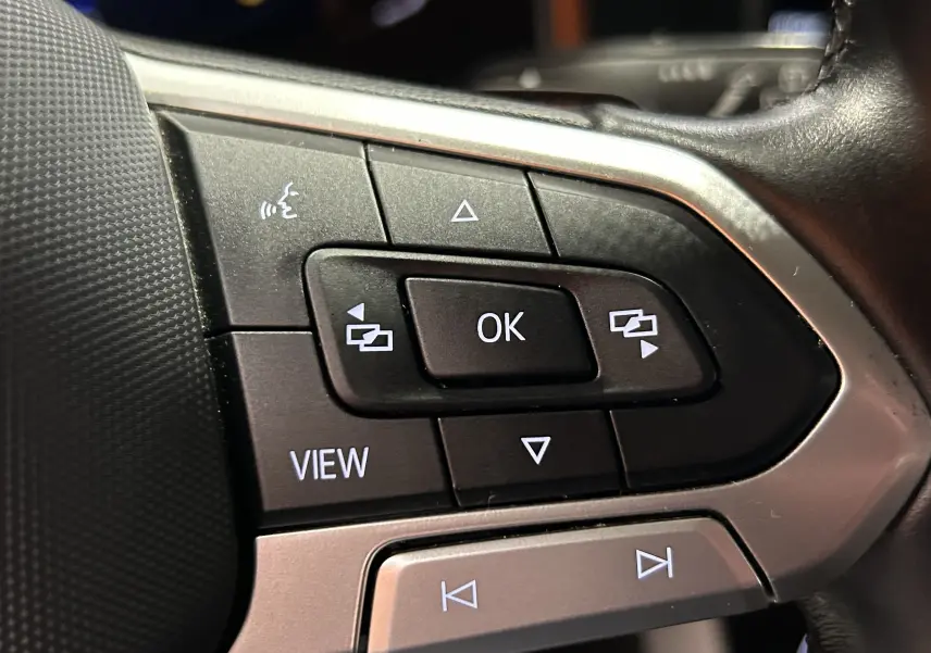 Gros plan sur les commandes multifonctions noires et argentées du volant de la Volkswagen Polo noire 2022.