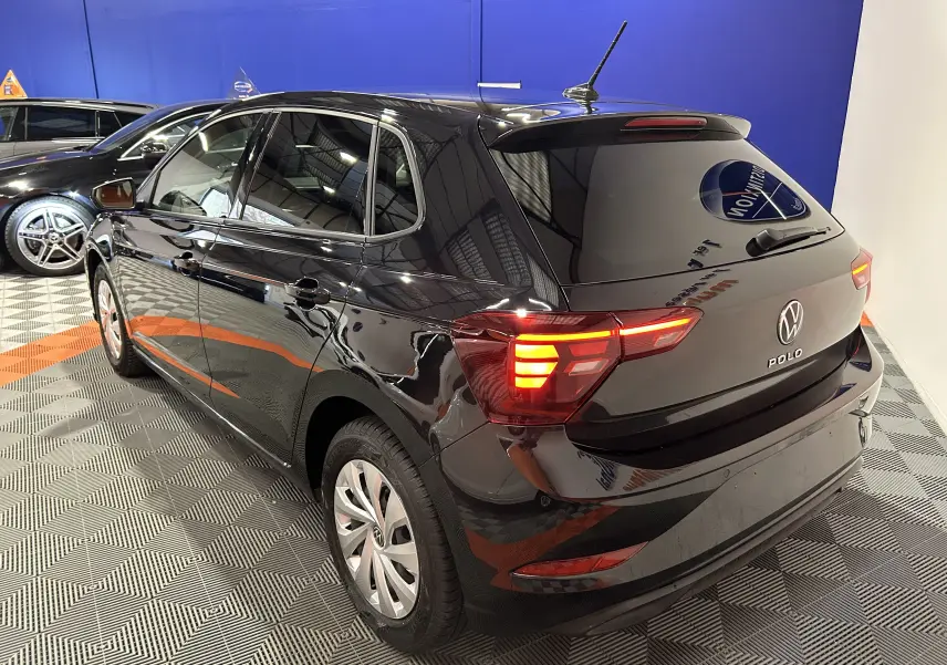 Vue 3/4 arrière droite d'une Volkswagen Polo noire 5 portes avec feux arrière allumés dans un showroom.