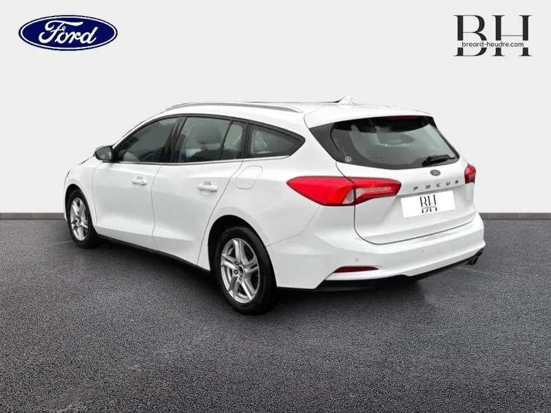 Vue 3/4 arrière droite d'une Ford Focus SW blanche Glacier avec jantes alu et barres de toit visibles.