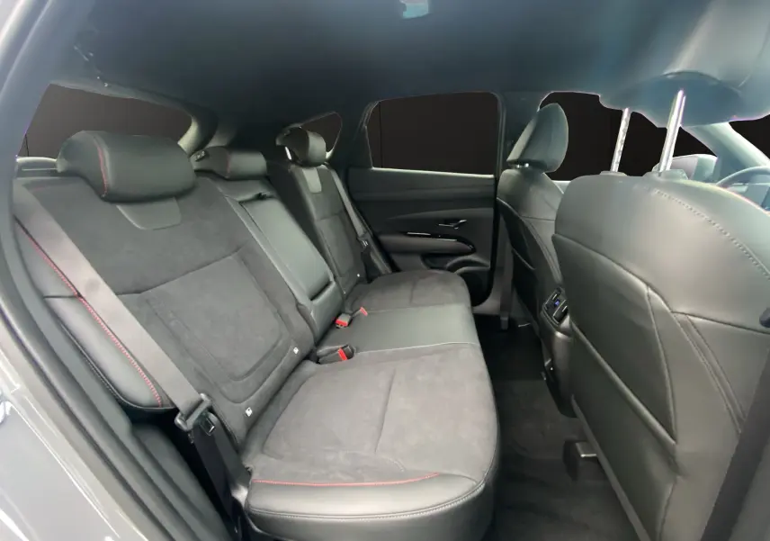 Vue intérieure arrière du Hyundai Tucson 2026 en Grey Shadow, sièges cuir noir/Alcantara avec surpiqûres rouges et vitres surteintées.