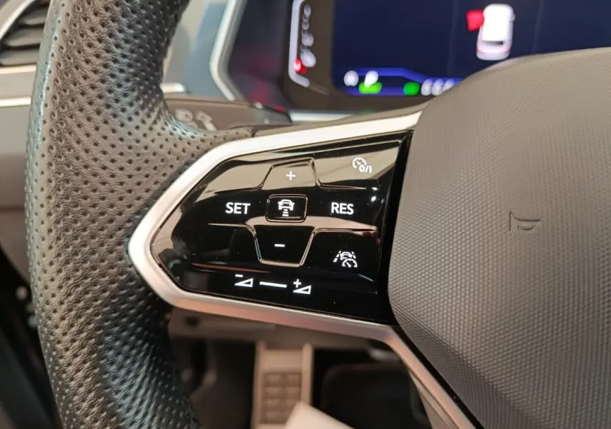 Gros plan sur le volant noir perforé du Volkswagen Tiguan 2023, avec commandes de régulateur adaptatif visibles.