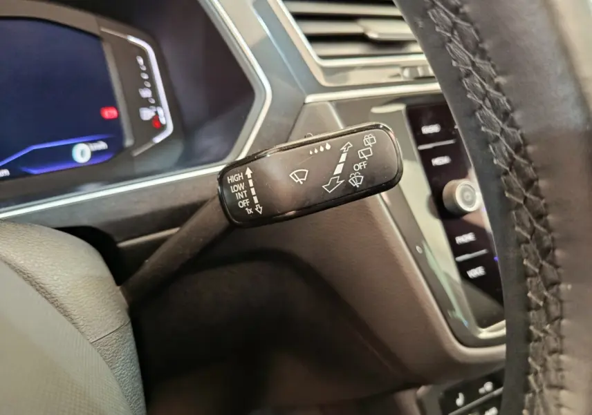 Gros plan sur le commodo d’essuie-glace noir dans l’habitacle du Volkswagen Tiguan noir, avec tableau de bord digital en arrière-plan.