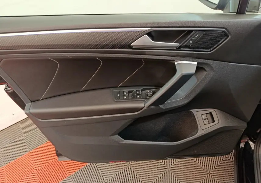 Vue intérieure de la porte avant gauche du Volkswagen Tiguan noir, avec commandes électriques et insert décoratif.
