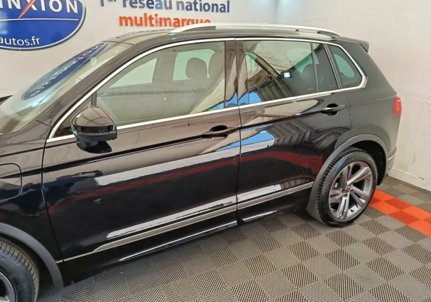 Vue latérale droite du Volkswagen Tiguan noir 2023 avec jantes alliage et rétroviseurs électriques dans un showroom.