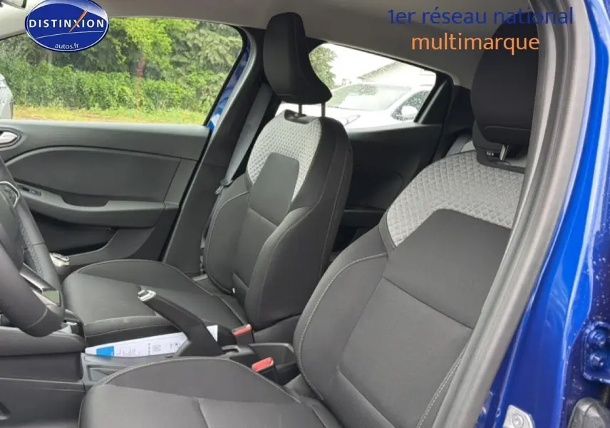Vue intérieure côté conducteur de la Renault Clio V bleu iron, mettant en valeur les sièges avant bicolores et la console centrale.