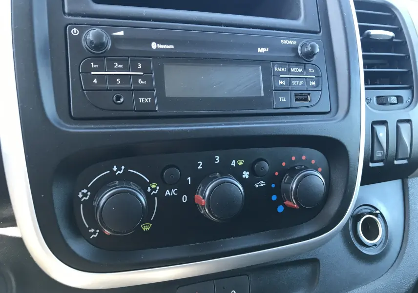 Gros plan sur la console centrale du Renault Trafic Fourgon blanc 2017, montrant les commandes de climatisation et radio.