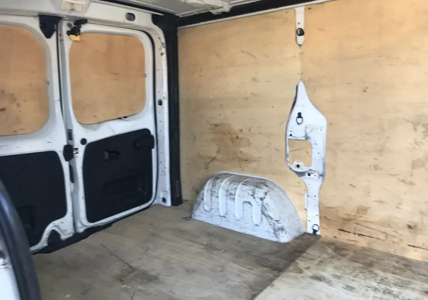 Intérieur du fourgon Renault Trafic blanc vu de l'arrière, montrant la zone de chargement avec parois en bois et traces d'usure.
