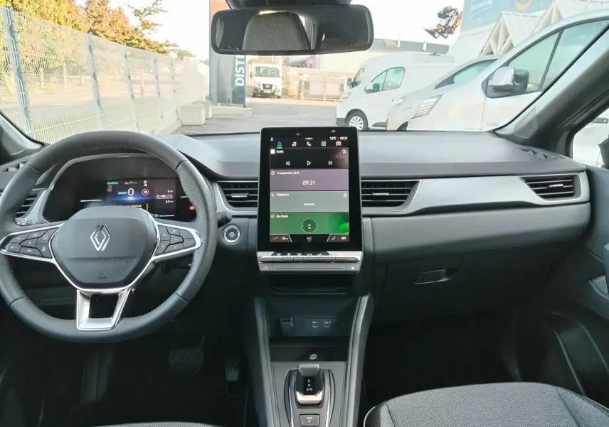 Vue intérieure frontale du Renault Captur E-Tech gris Cassiopée, tableau de bord moderne avec écran tactile vertical et volant multifonction.