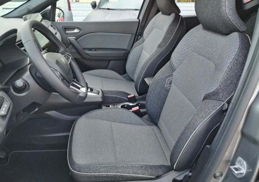 Vue intérieure côté conducteur du Renault Captur 2025, sièges tissu gris avec surpiqûres blanches et volant cuir noir.