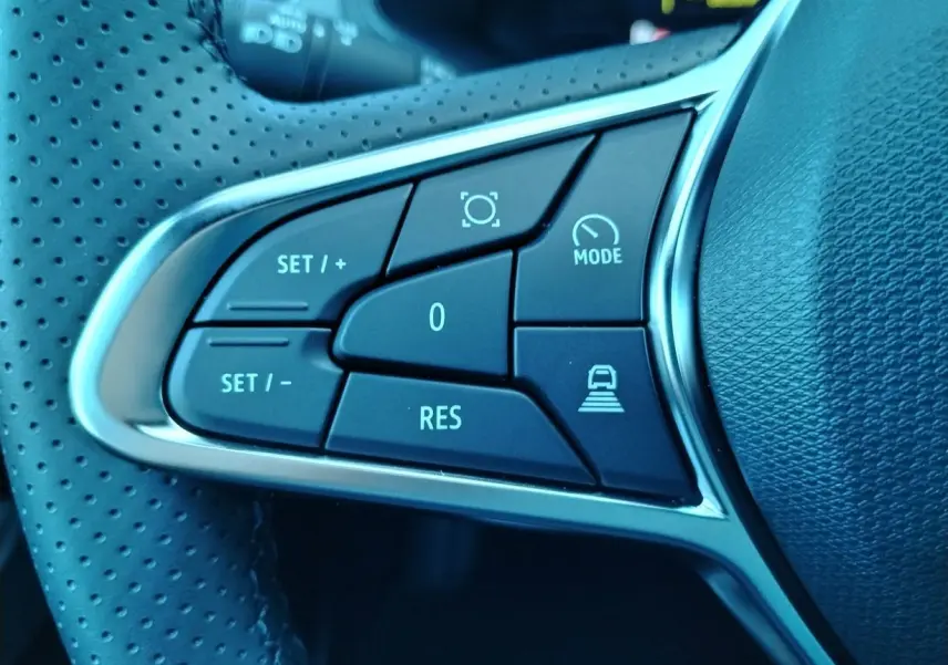 Gros plan sur les commandes du volant perforé du Renault Captur E-Tech gris cassiopée, boutons de régulateur et mode de conduite.