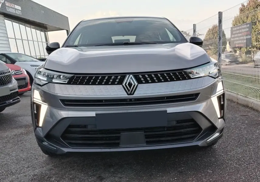 Vue frontale du Renault Captur E-Tech gris Cassiopée avec toit noir, feux LED verticaux allumés, calandre moderne.