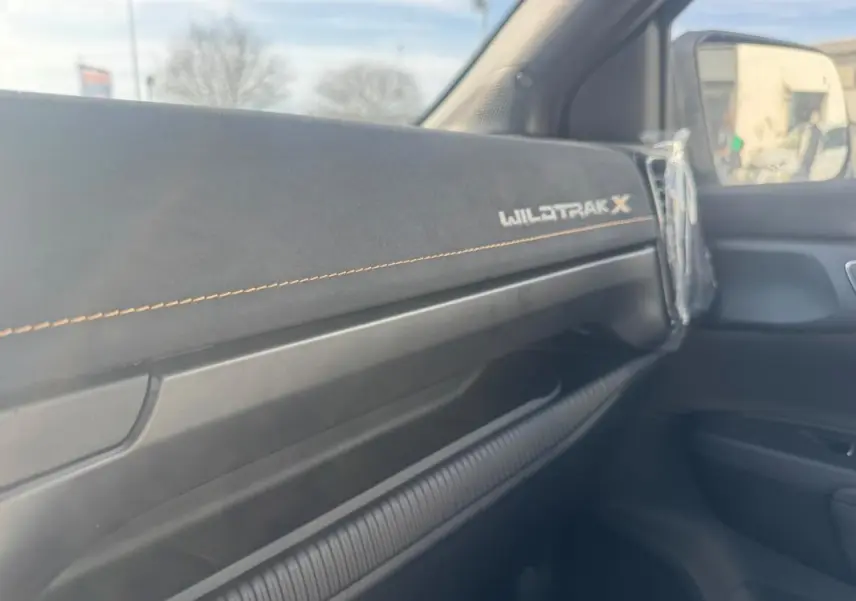 Intérieur côté passager du Ford Ranger Wildtrak X 2025, tableau de bord noir avec surpiqûres orange et logo brodé.
