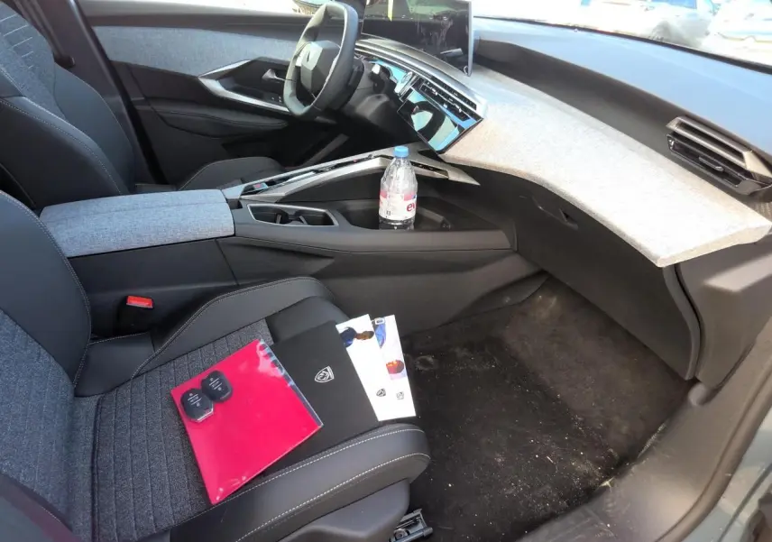 Intérieur avant droit du Peugeot 3008 2025, tableau de bord clair avec écran incurvé et sièges tissu gris foncé.