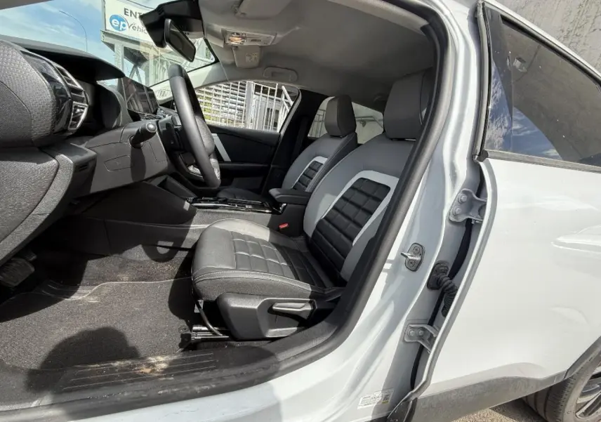 Vue côté conducteur intérieur de la Citroën C4 blanc okenite 2025, sièges bi-matière noirs et gris avec console centrale visible.