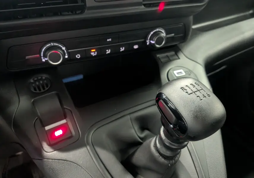 Gros plan sur le levier de vitesses manuel noir du Citroën Berlingo blanc, avec la console centrale et commandes de climatisation visibles.