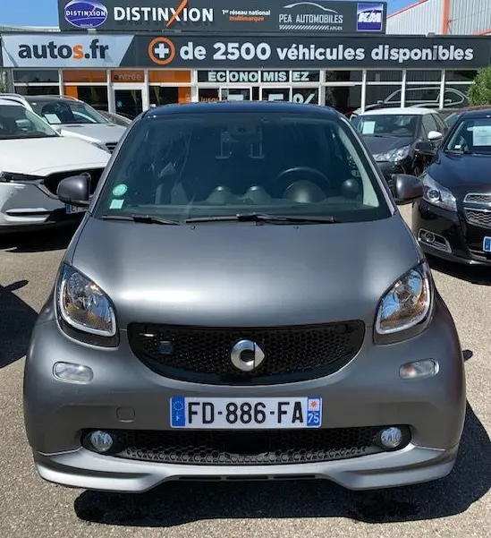 Vue avant d'une Smart Fortwo Coupé électrique gris mat, version Brabus Style, stationnée en extérieur devant un concessionnaire.