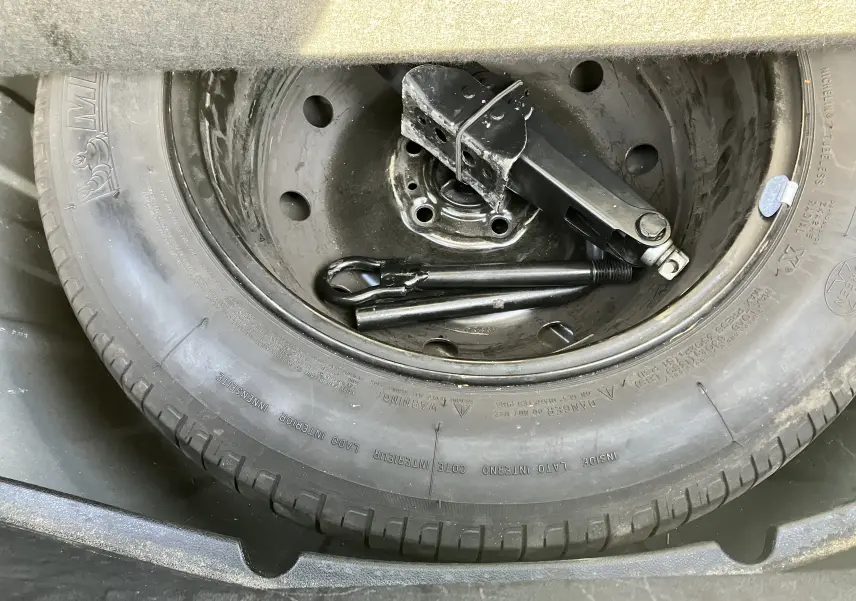 Gros plan sur la roue de secours noire d'une Renault Laguna 1.5l dci 110 ch, avec cric et outils de levage rangés à l'intérieur.