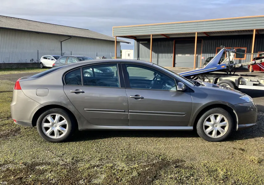 Profil côté gauche d'une Renault Laguna gris vert de 2008, berline 5 portes avec jantes alliage et vitres légèrement teintées.