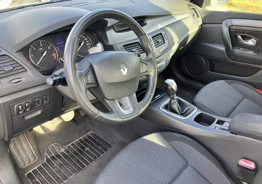 Intérieur noir de la Renault Laguna 2008, vue côté conducteur sur le volant, levier de vitesse manuel et tableau de bord.