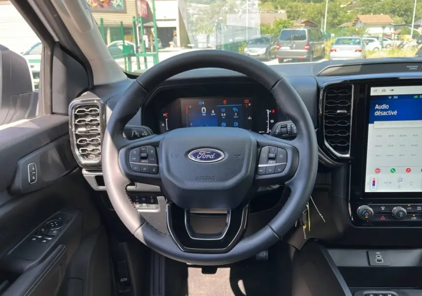 Vue intérieure centrée sur le volant cuir multifonctions du Ford Ranger blanc glacier avec écran tactile et tableau de bord numérique.