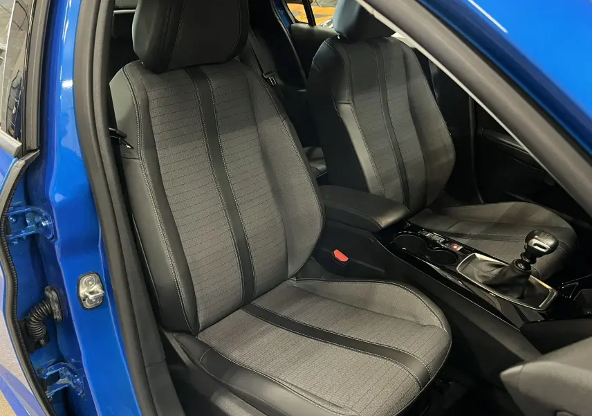 Vue intérieure côté conducteur de la Peugeot 208 Bleu Vertigo avec sièges gris et levier de vitesse manuel visible.