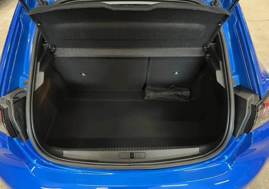 Coffre ouvert vu de dessus d’une Peugeot 208 Bleu Vertigo, montrant un espace de rangement vide et propre.