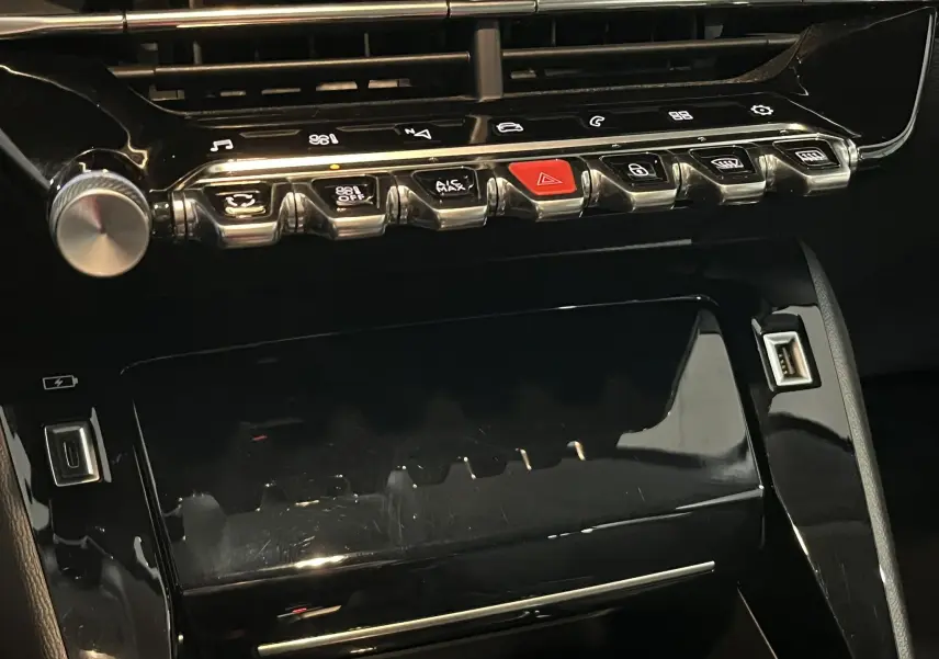 Gros plan sur la console centrale noire brillante de la Peugeot 208 1.5 BlueHDi, avec boutons de commande et prise USB visible.