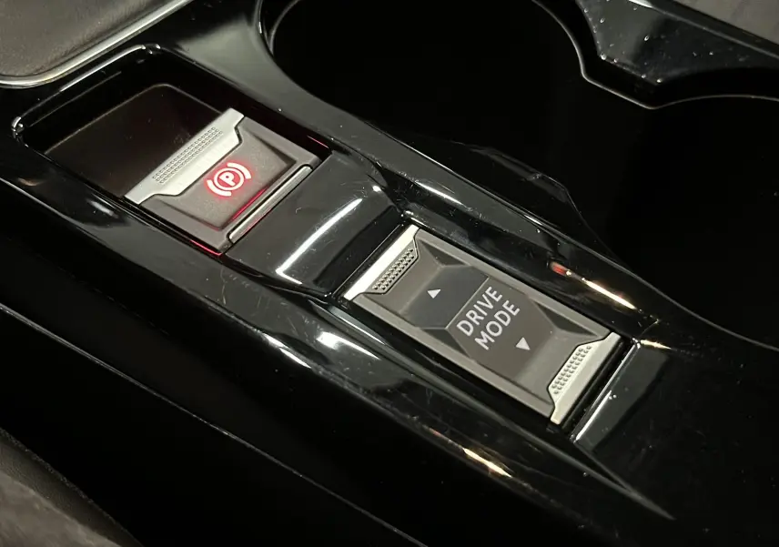 Gros plan sur la console centrale noire brillante de la Peugeot 208 1.5 BlueHDi, avec bouton frein à main électronique et sélection drive mode.