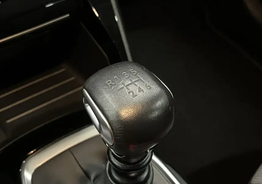 Gros plan sur le levier de vitesses manuel noir de la Peugeot 208 1.5 BlueHDi, intérieur sombre.