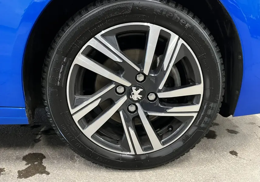 Gros plan sur la roue avant gauche d’une Peugeot 208 Bleu Vertigo, avec jante alliage bicolore et logo lion au centre.
