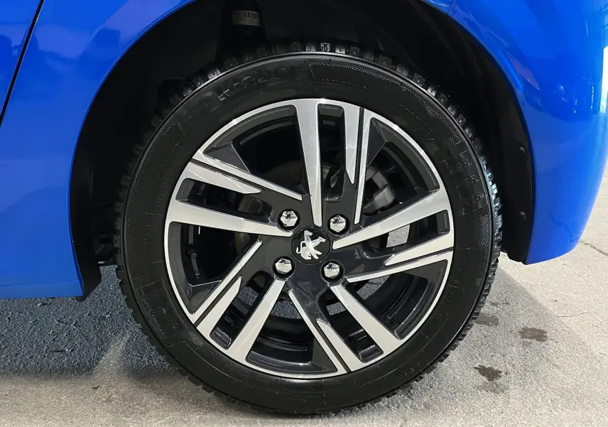 Gros plan sur la roue avant droite d'une Peugeot 208 Bleu Vertigo avec jante alliage bicolore moderne.