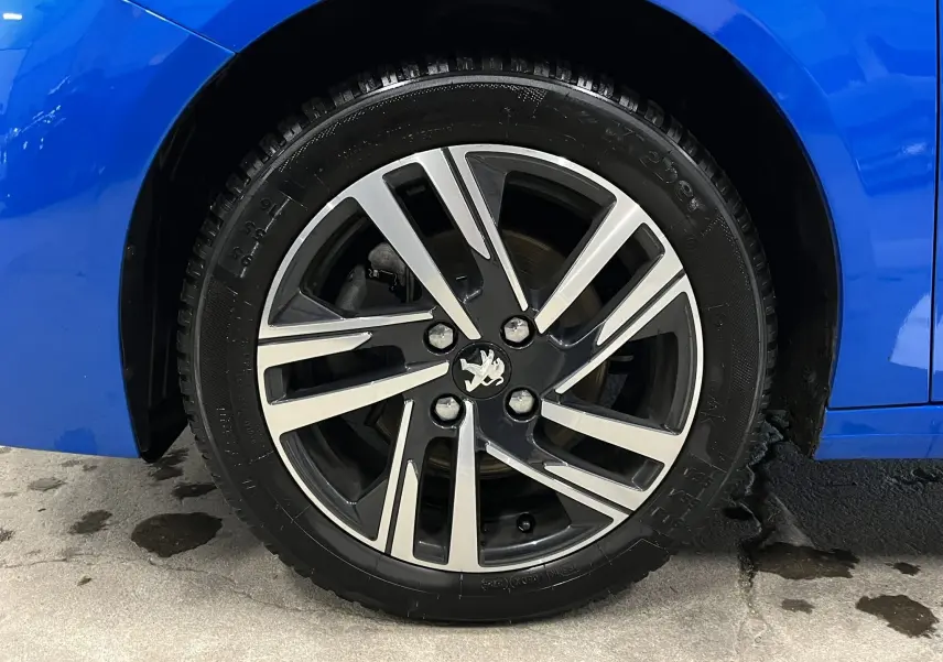 Gros plan sur la roue avant gauche de la Peugeot 208 Bleu Vertigo avec jante alliage bicolore distinctive.