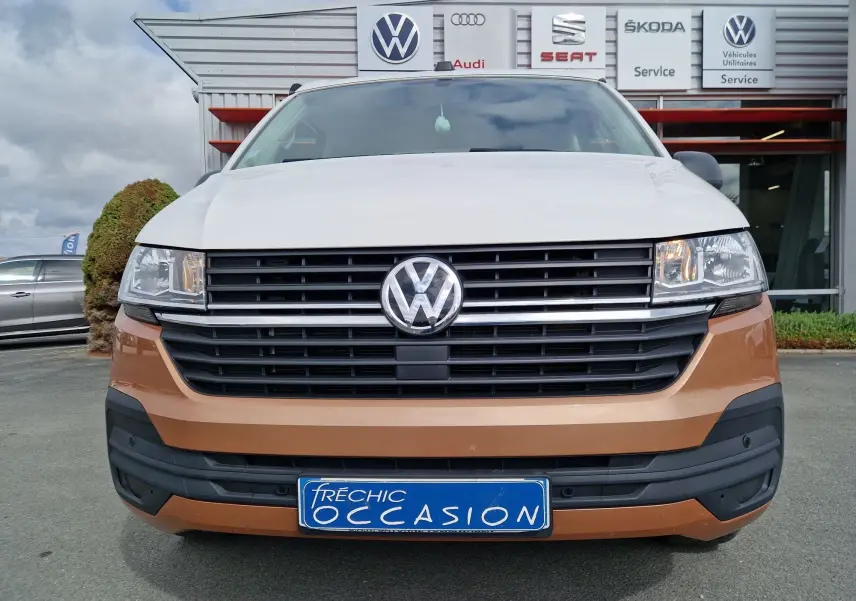 Vue frontale d'un Volkswagen California Cooper bronze et blanc, avec plaque d'occasion bleue visible au centre.