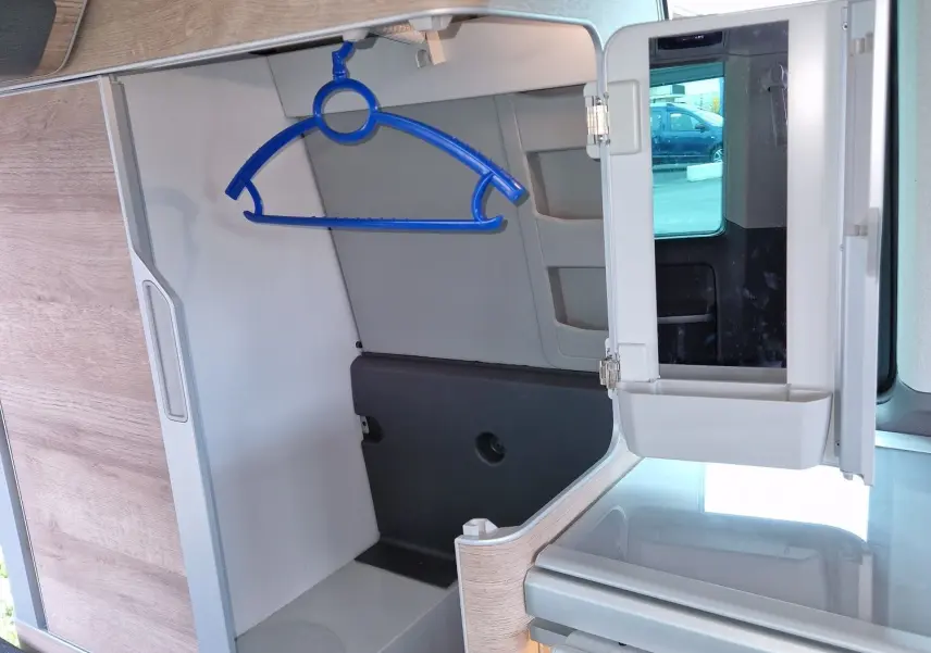 Intérieur du Volkswagen California 2021 en Cooper bronze, vue sur le placard ouvert avec un cintre bleu et un miroir rabattable.