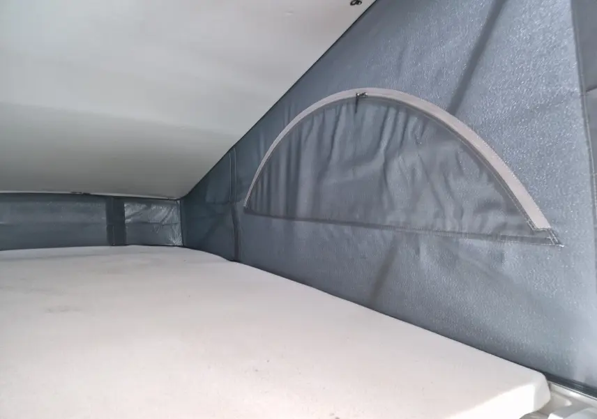 Détail intérieur du couchage avec fenêtre en demi-lune dans le toit relevable du Volkswagen California Cooper bronze.