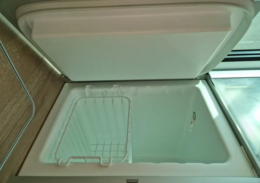 Intérieur du réfrigérateur ouvert du Volkswagen California 2021, montrant un compartiment blanc avec panier métallique.