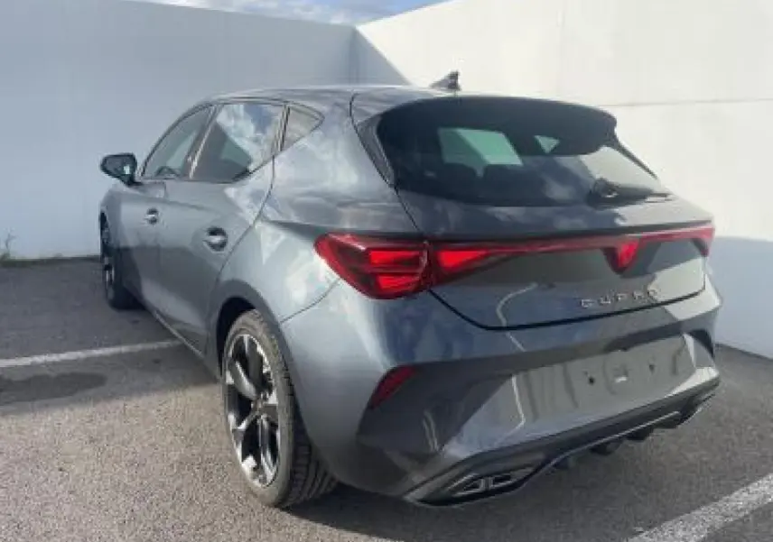 Vue 3/4 arrière droite d'une CUPRA Leon 2025 gris magnetic metal avec bandeau lumineux arrière et jantes alliage noires.