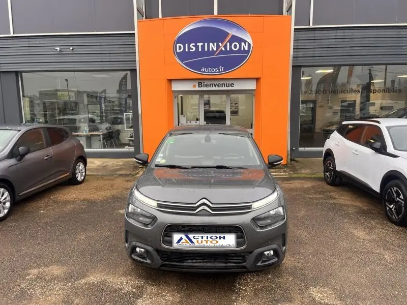 Vue avant d'une Citroën C4 Cactus gris Platinium, avec calandre distinctive et phares LED, devant un garage orange.
