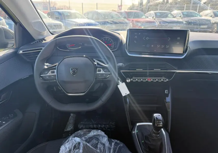 Vue intérieure frontale du poste de conduite d'une Peugeot 208 jaune 2025 avec volant multifonction et écran tactile.