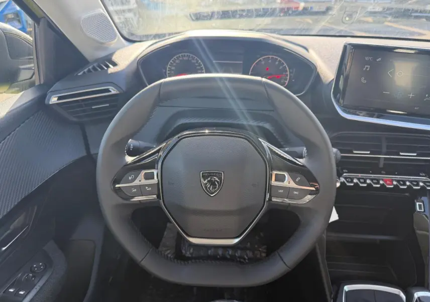 Vue intérieure centrée sur le volant compact de la Peugeot 208 2025 avec tableau de bord et écran tactile visibles.