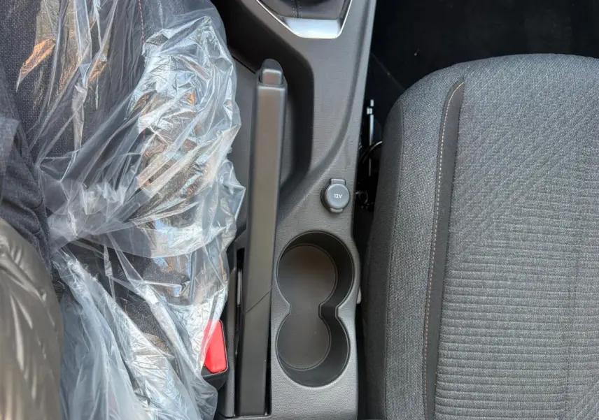 Vue rapprochée de la console centrale noire avec frein à main, prise 12V et siège tissu gris de la Peugeot 208 jaune.