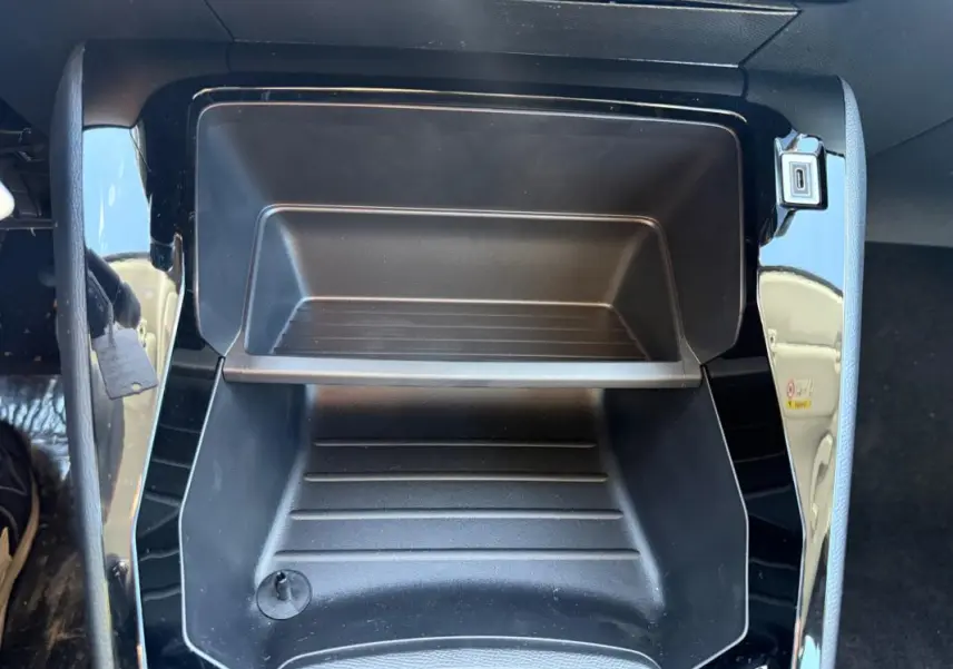 Gros plan sur le rangement central noir brillant de la Peugeot 208 jaune 2025, avec prise USB visible.