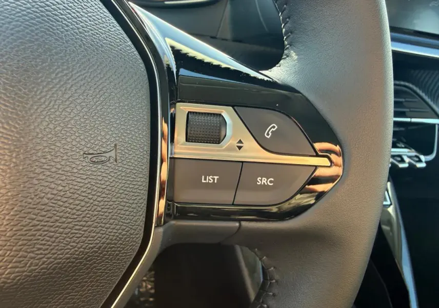 Gros plan sur les commandes gauche du volant noir de la Peugeot 208 jaune, avec boutons LIST, SRC et téléphone.