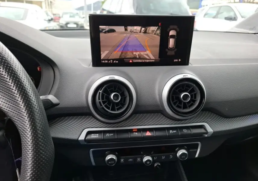 Vue intérieure du tableau de bord noir d'Audi Q2 2023 avec écran affichant la caméra de recul et aérateurs ronds centraux.