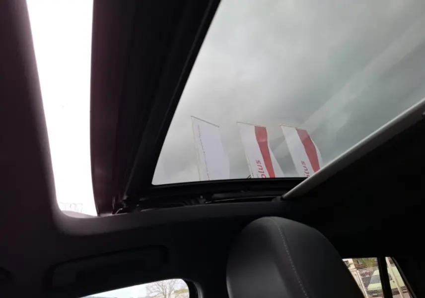 Vue intérieure du toit ouvrant panoramique ouvert sur Audi Q2 noir, avec appui-tête avant visible et ciel nuageux.